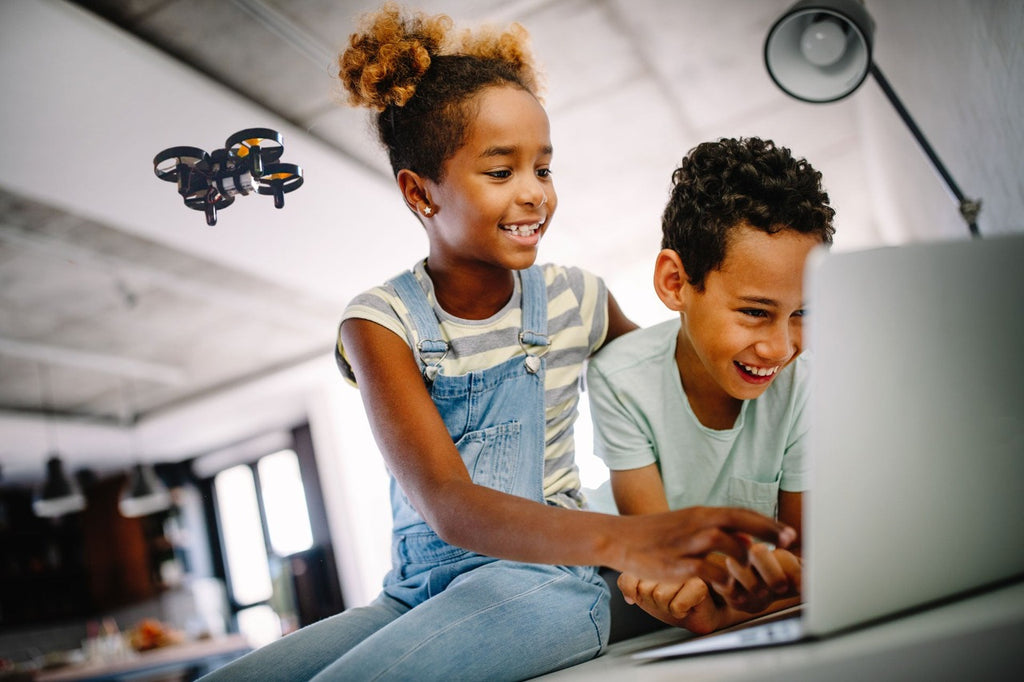 A girl and boy using a laptop to code the CoDrone Mini to do a takeoff in their kitchen