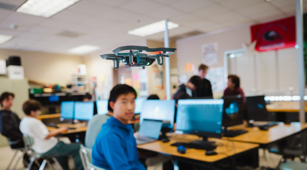 Students in a high school classroom watching a small drone fly